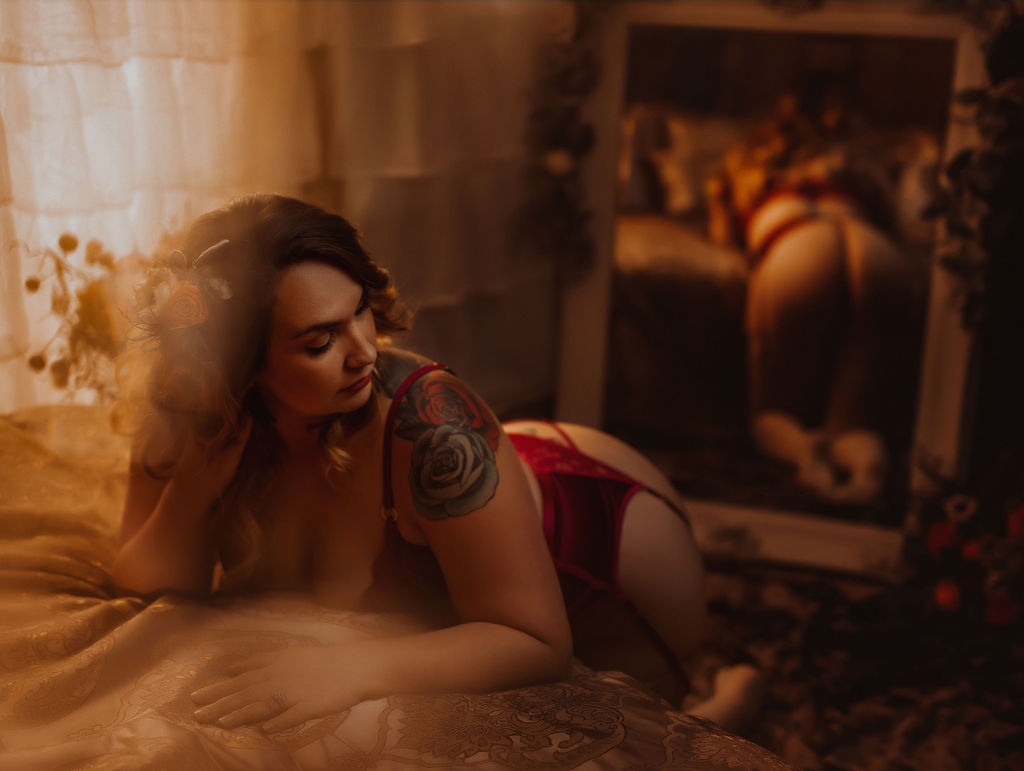 woman in red lingerie leaning over a bed with a mirror behind her